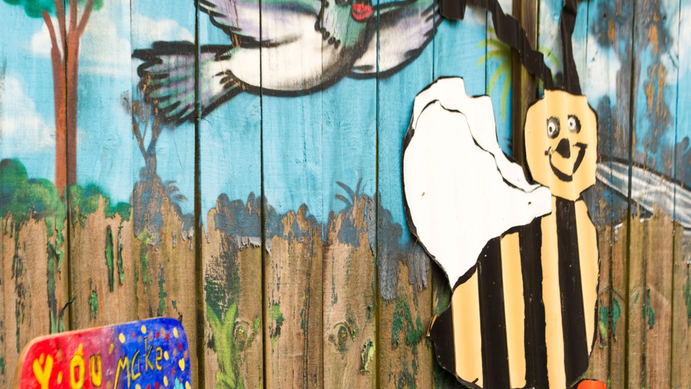 A mural of a bumble bee and a bird on a fence.