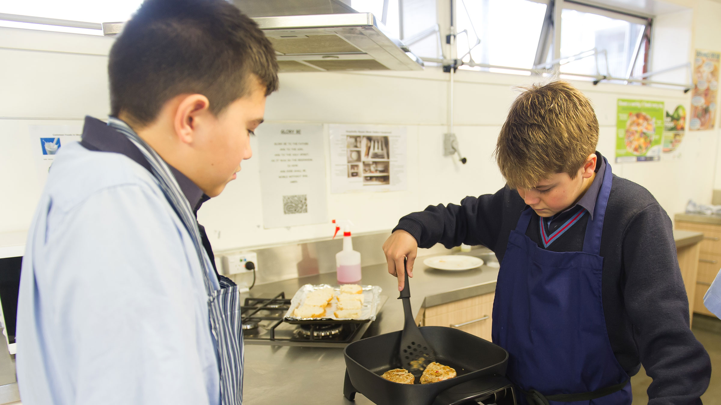 Two boys cooking with an electric frying pan.