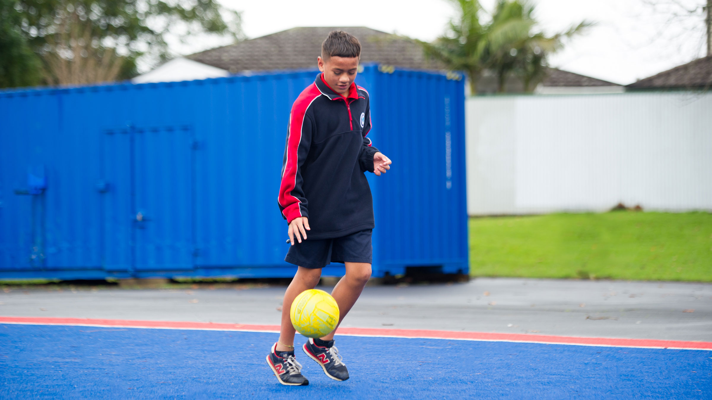 An intermediate-aged student dribbling a football outdoors