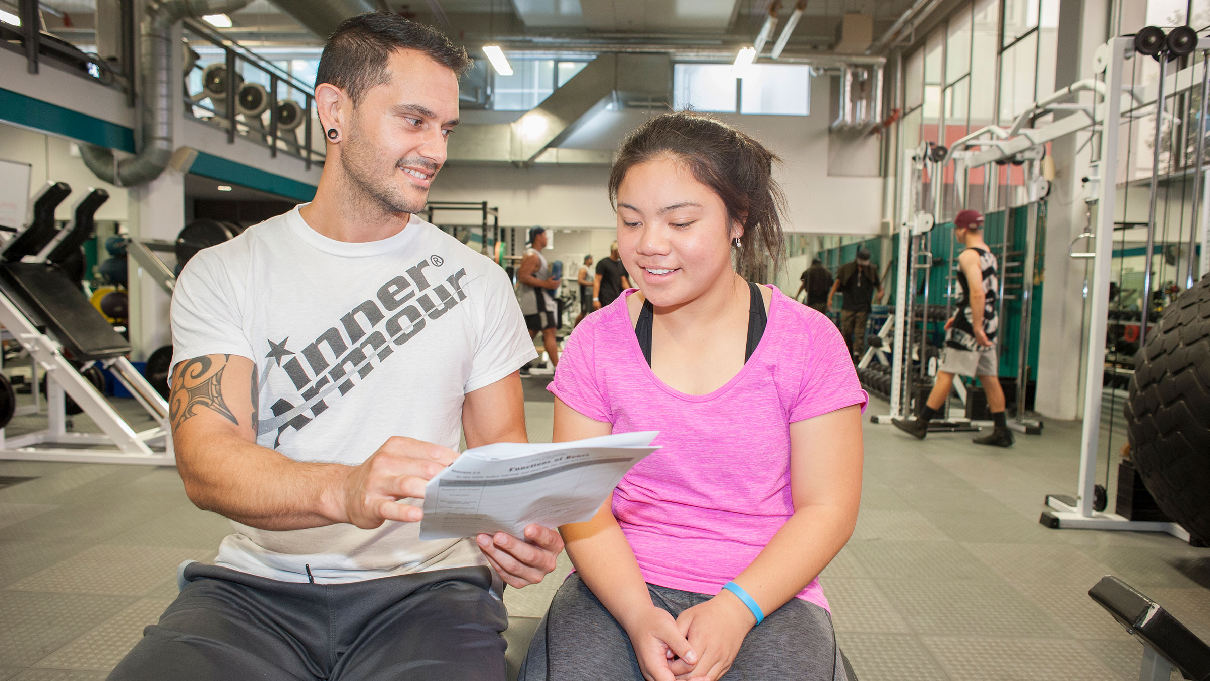 A teacher and student in a gym, discussing a worksheet