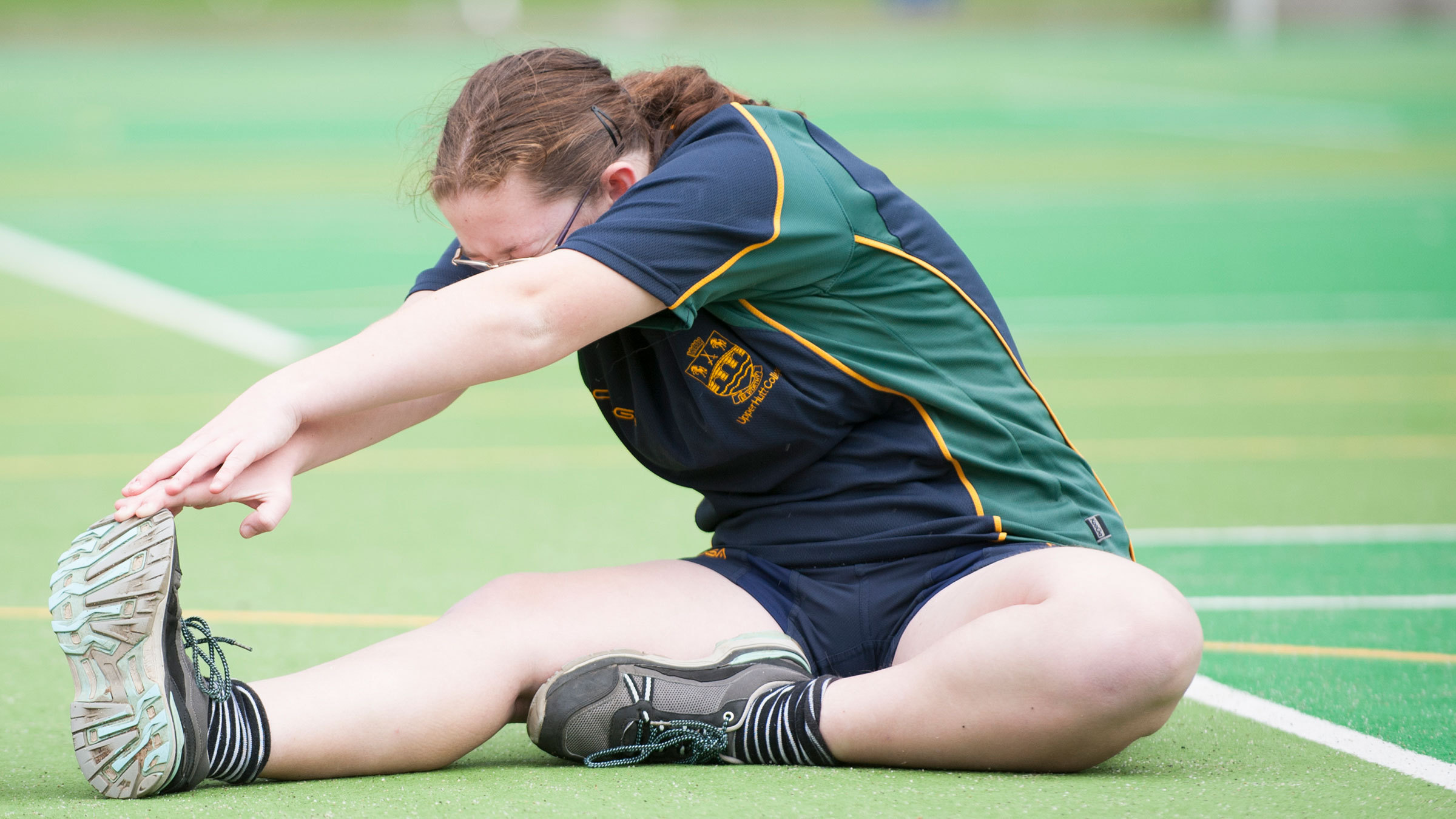 A teenage student stretching on a green court