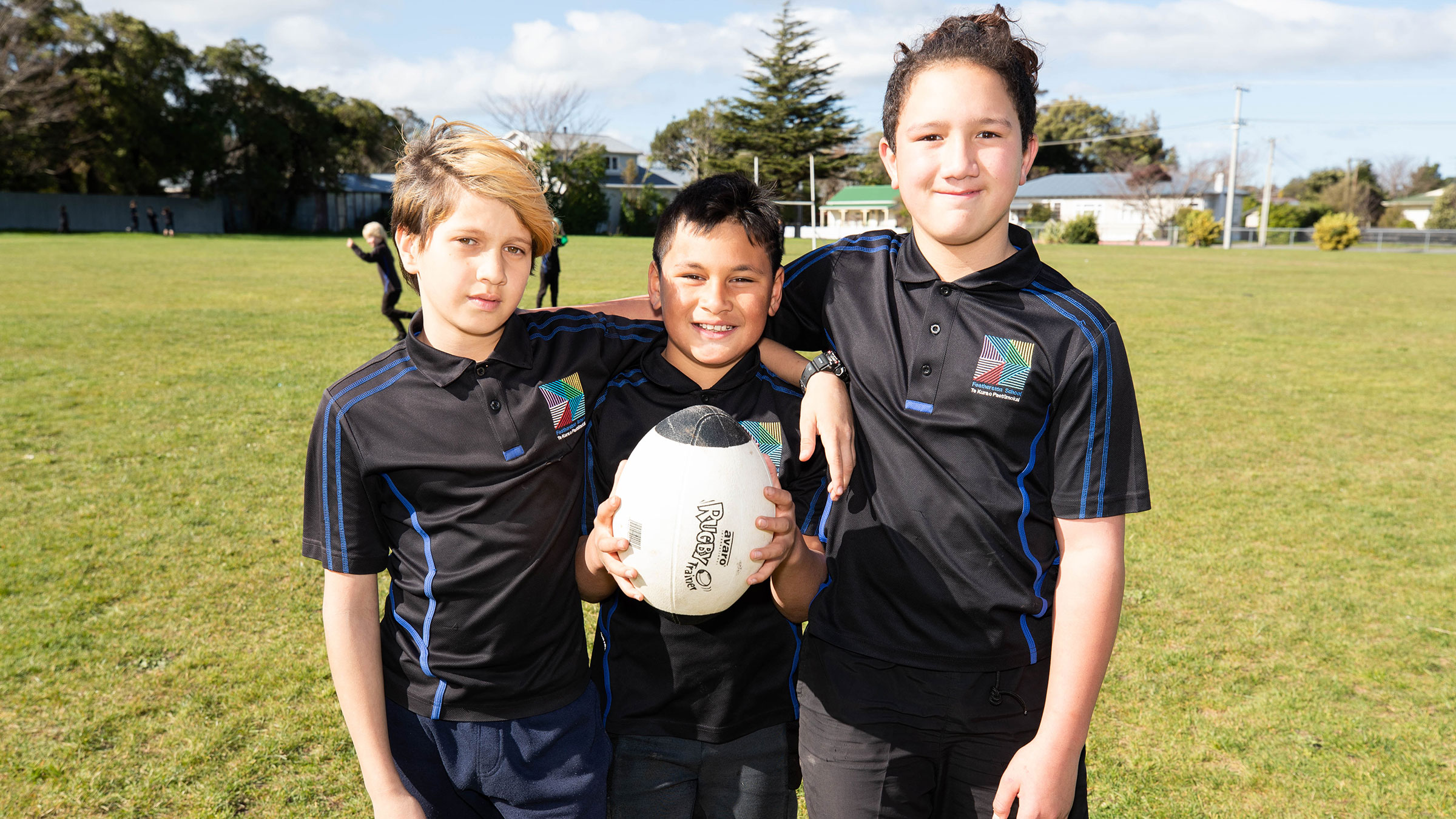 Three students in sport uniforms posing with a rugby ball and smiling