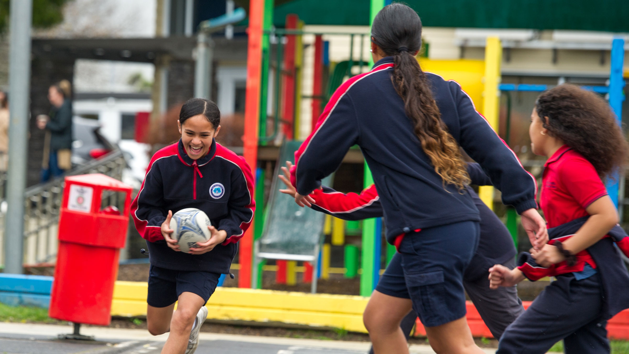 A girl running with a rugby ball towards a group of students