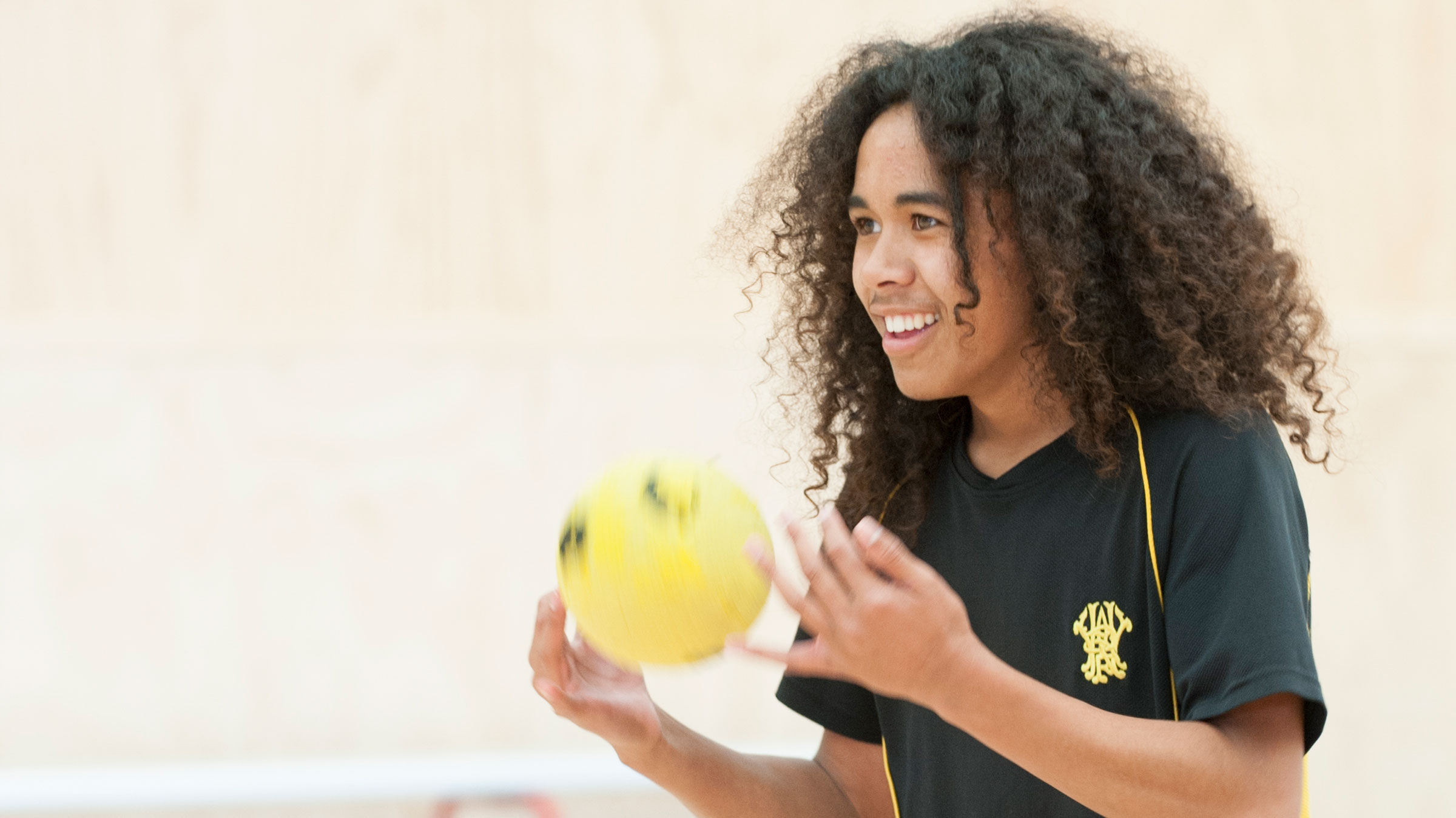 A teenager tossing a yellow ball and smiling