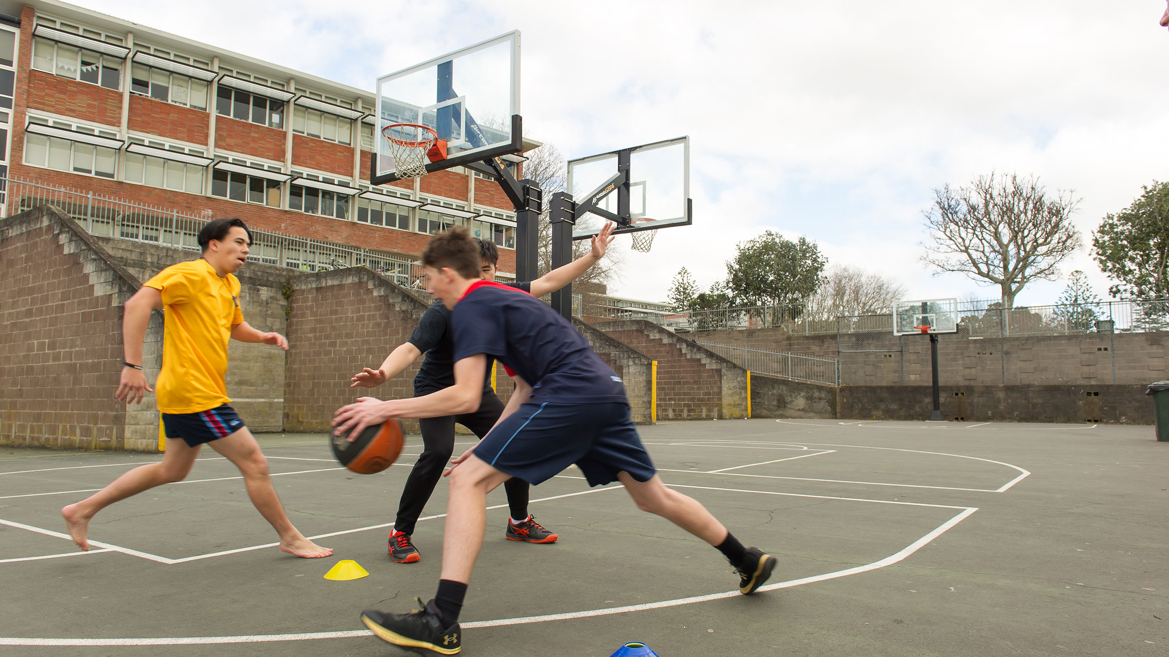 The teenage boys playing basketball on an asphalt court